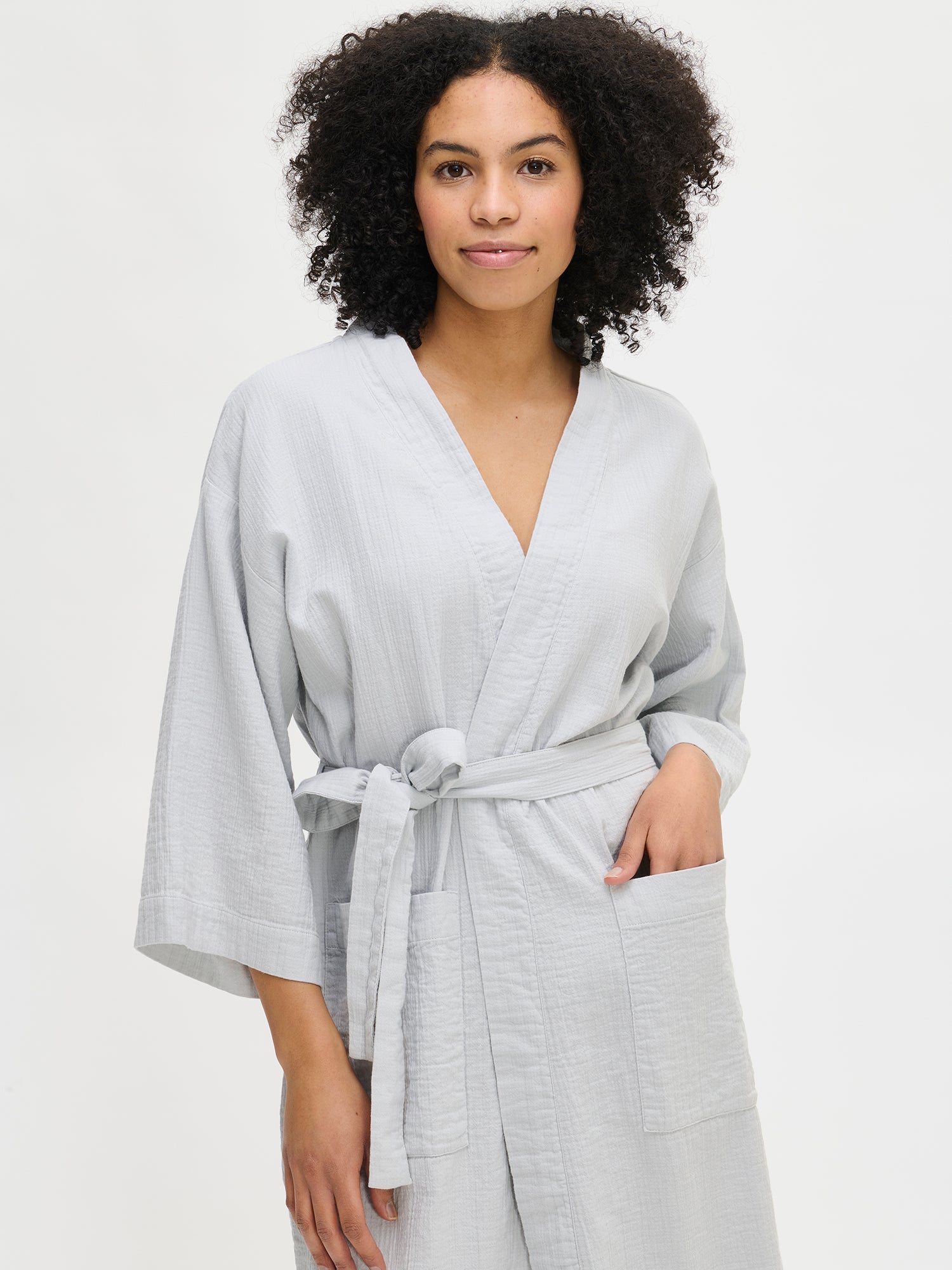 Nanso women's comfortable solid blue Aamu bathrobe with a knee-length hem, featuring kimono-style sleeves, a neckline finished with a wide trim, patch pockets, and a belt attached with belt loops, worn by the model in a close-up front view.
