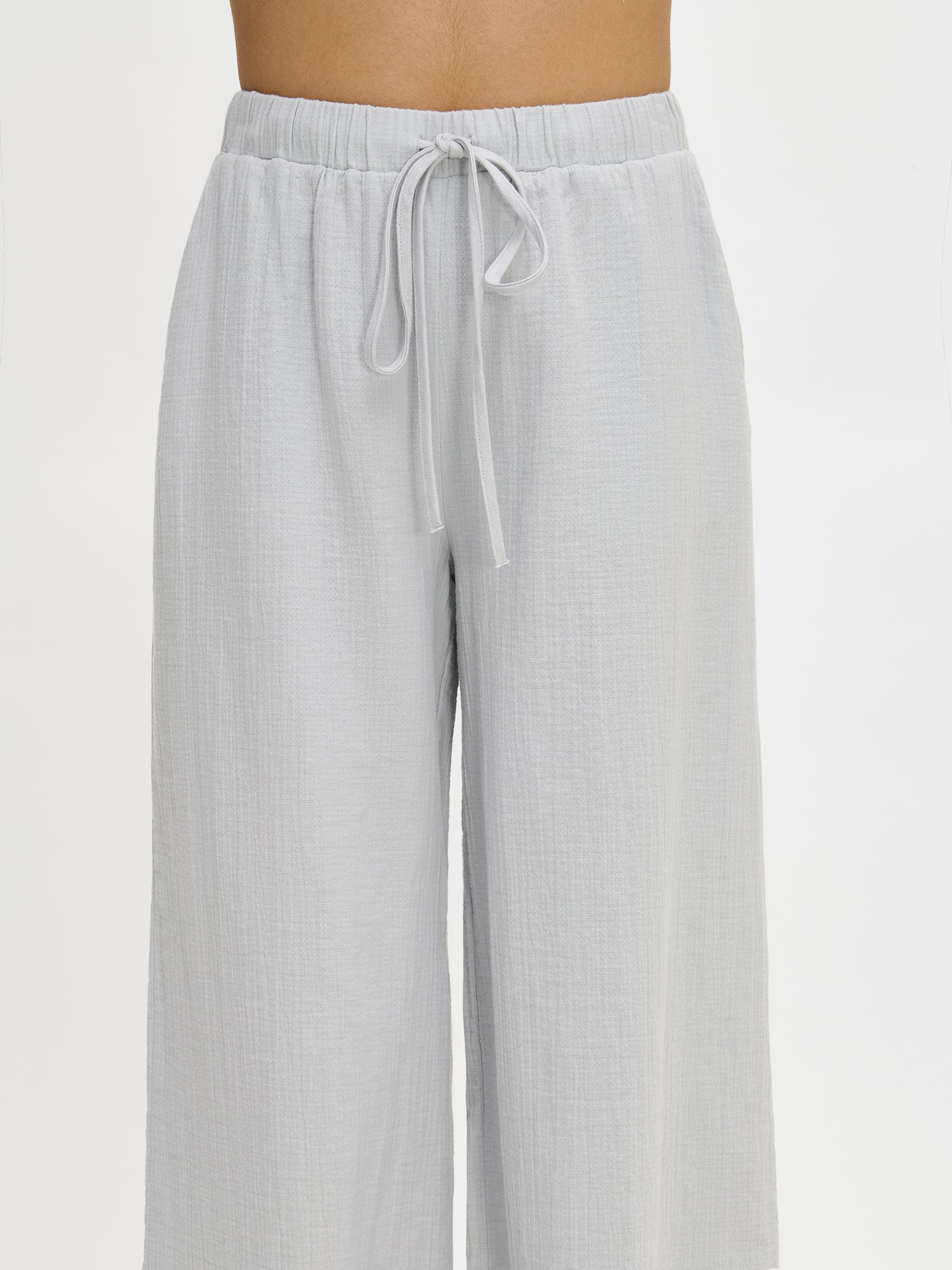 Nanso women's relaxed, wide-leg, solid blue Aamu pants with side pockets, a comfortable elastic waistband with a drawstring, and 7/8-length legs, worn by the model in a close-up front view.