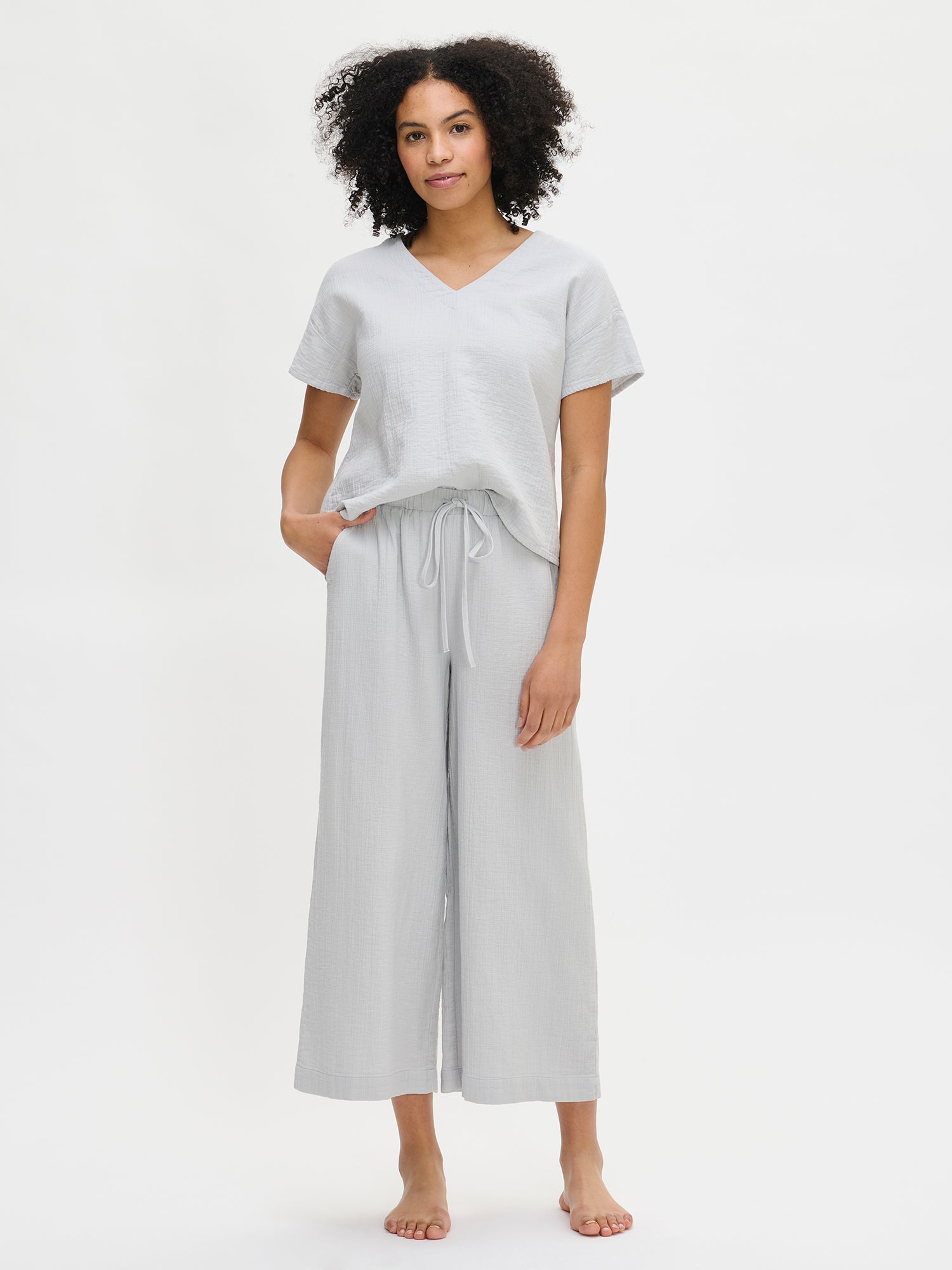Nanso women's relaxed, wide-leg, solid blue Aamu pants with side pockets, a comfortable elastic waistband with a drawstring, and 7/8-length legs, worn by the model in a front view.