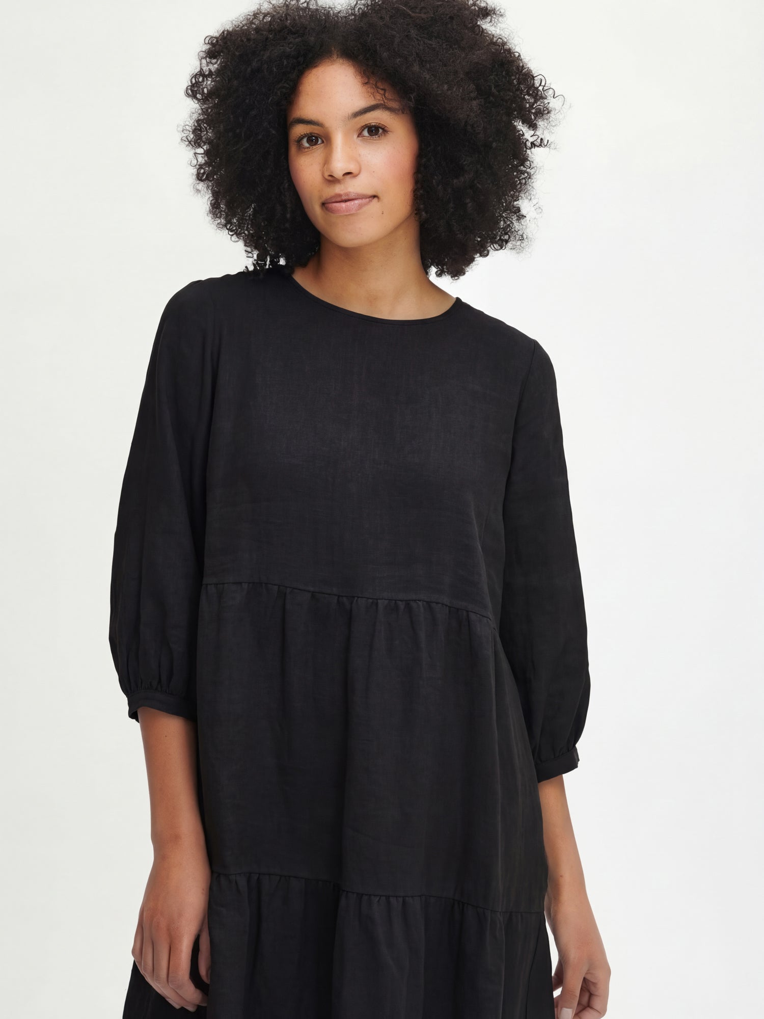 Women's Saralia Linen Dress in black features voluminous frill layers, 3/4 length sleeves that gracefully gather above the cuff with button adjusters for a tailored fit. Pictured on a model, close-up.