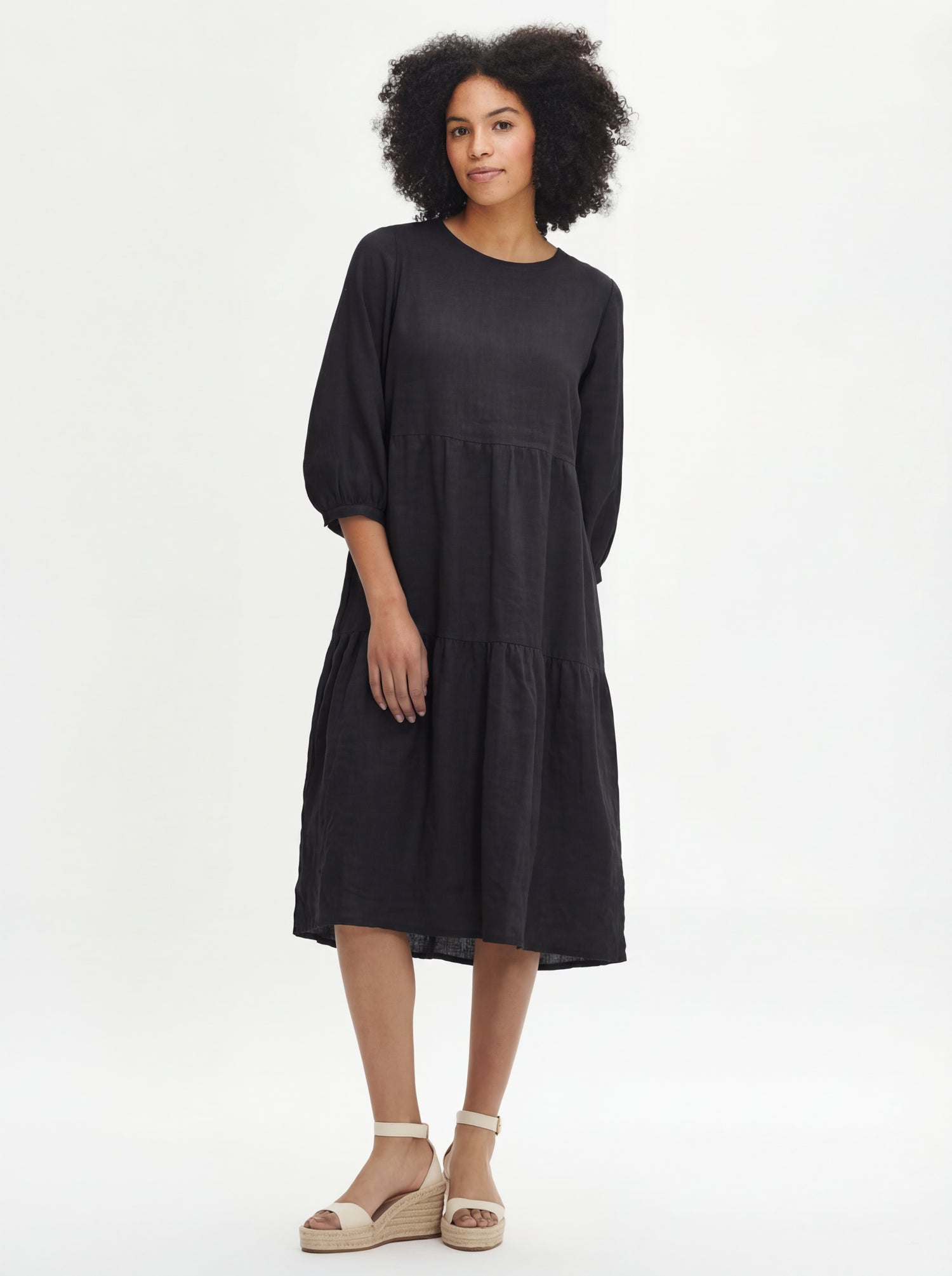 Women's Saralia Linen Dress in black features voluminous frill layers, 3/4 length sleeves that gracefully gather above the cuff with button adjusters for a tailored fit. Pictured on a model.