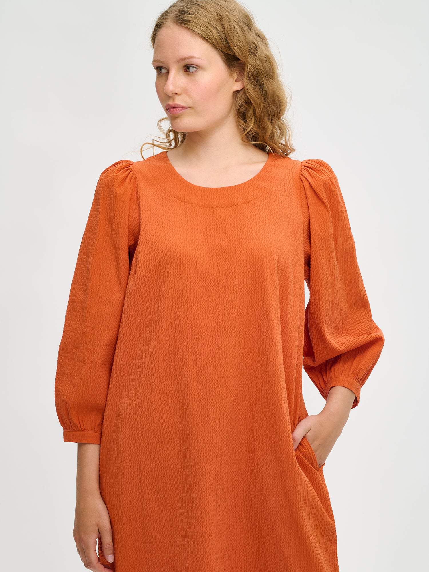 Nanso women’s solid orange Bianca dress in cotton–elastane, round neckline and gathered sleeves, knee-length, worn by model in close-up view.