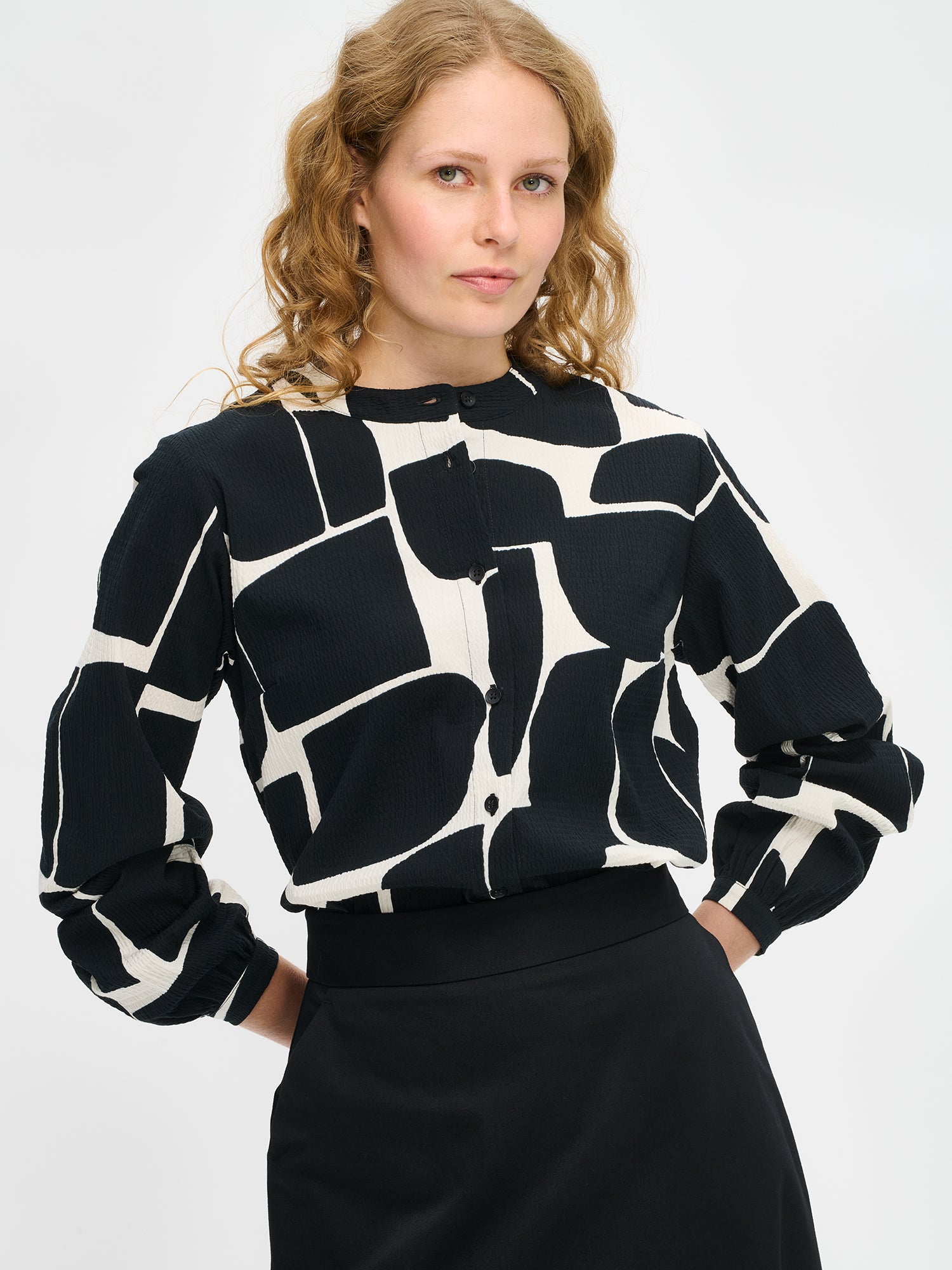 Nanso women’s black and white patterned Muuri shirt in woven cotton, straight hem with collar and button closure, hip-length, worn by model in close-up view.