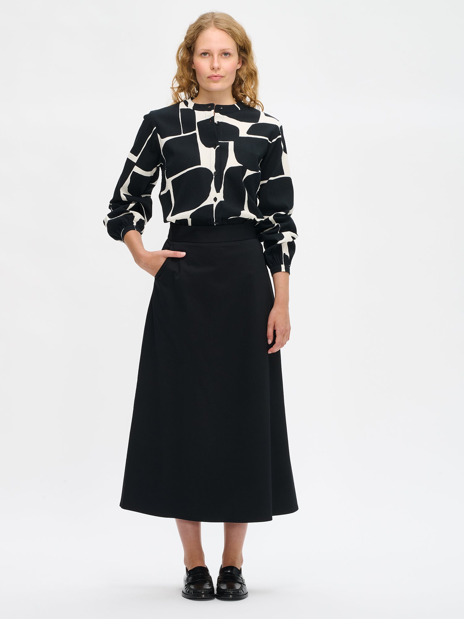 Nanso women’s black and white patterned Muuri shirt in cotton blend, collar and buttons, long gathered sleeves, hip-length fit, worn by model in full-body view.