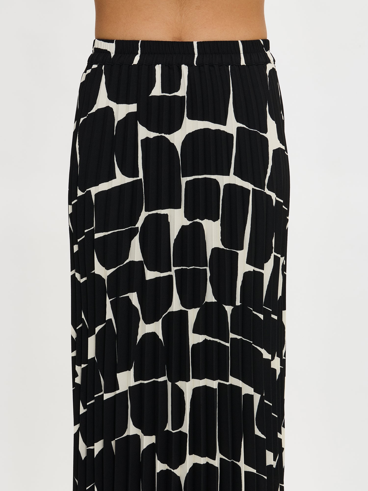 Nanso women’s black and white patterned Muuri skirt in easy-care polyester, fine pleats, worn by model close-up from waist down.