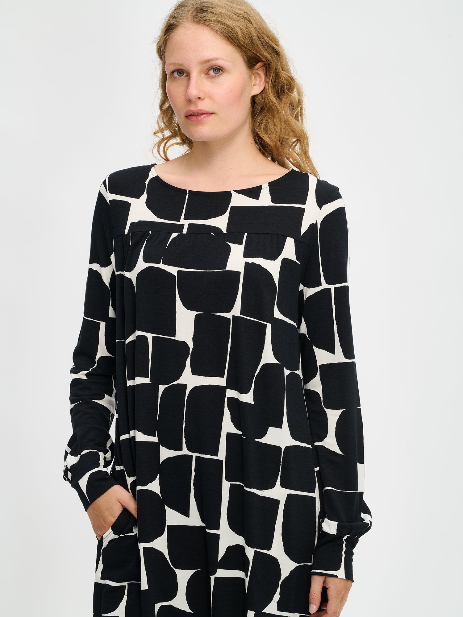 Nanso women’s black and white patterned Muuri tunic in viscose–elastane knit, round neckline with gathered yoke and pockets, worn by model in mid close-up.