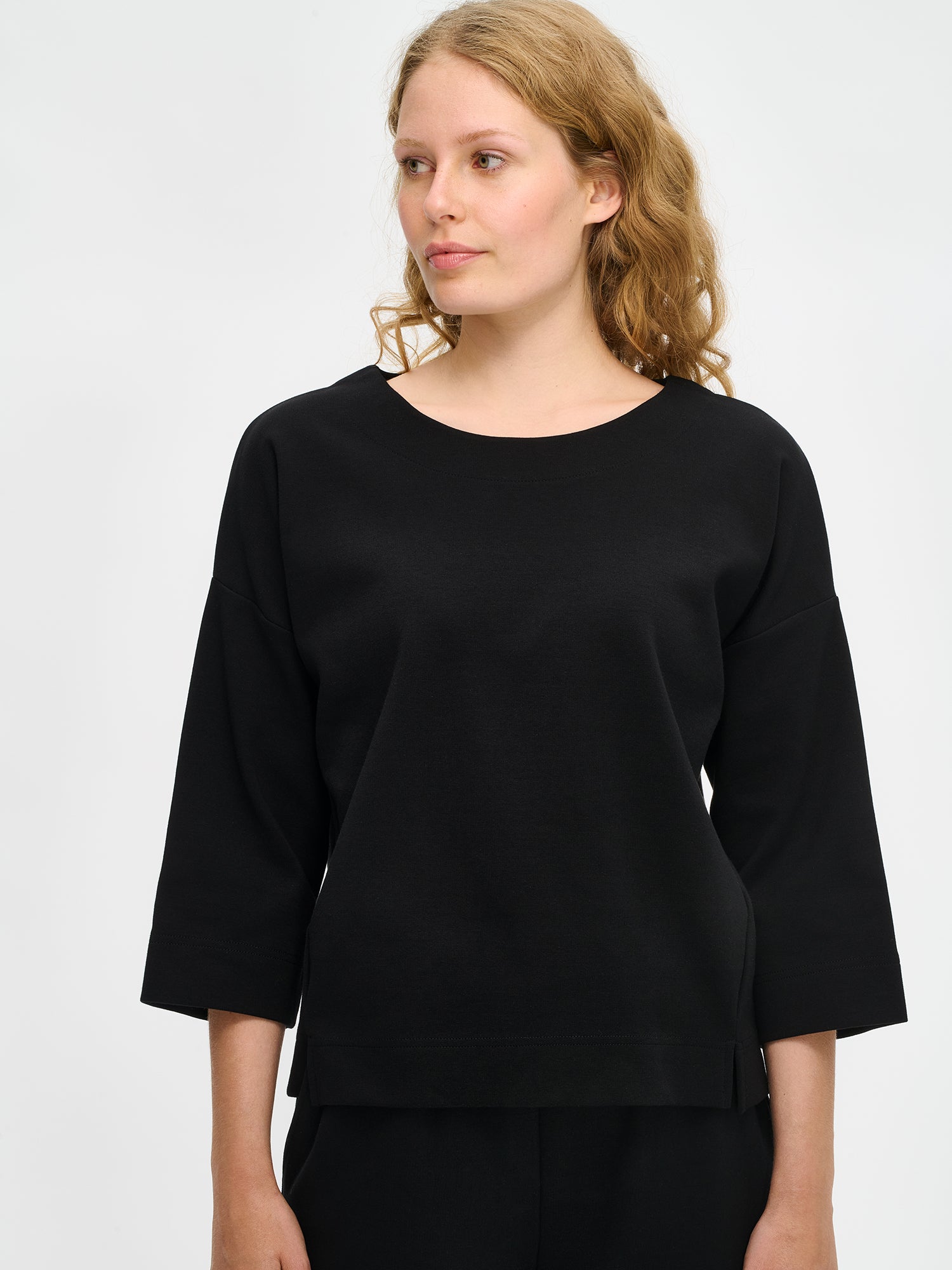 Nanso women’s black Elena top in stretch cotton blend, oval neckline, 3/4 sleeves and side slits, worn by model in close-up view.