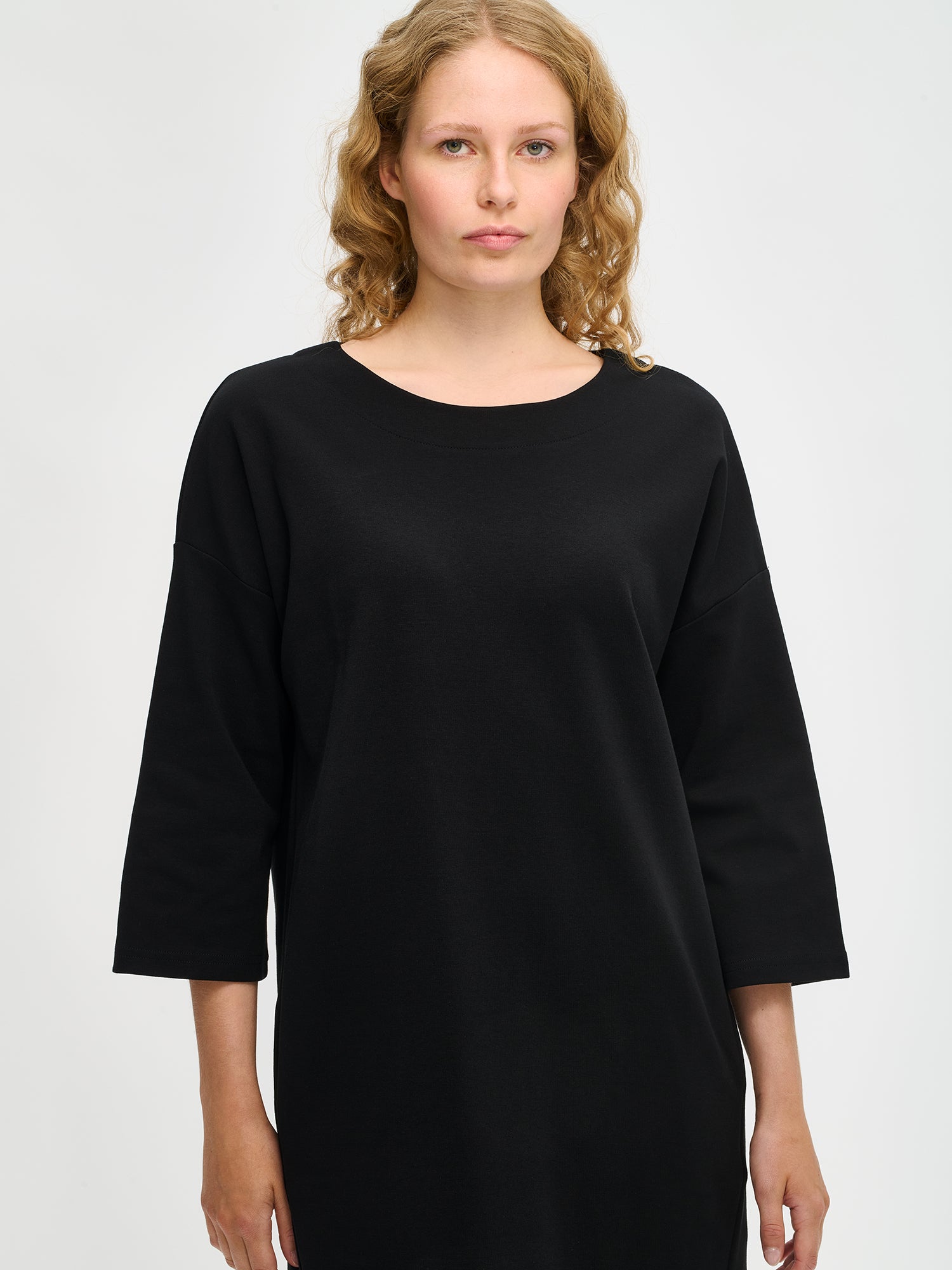 Nanso women’s black Elena knit dress in stretch cotton blend, oval neckline and 3/4 sleeves, relaxed straight fit, worn by model in close-up view.