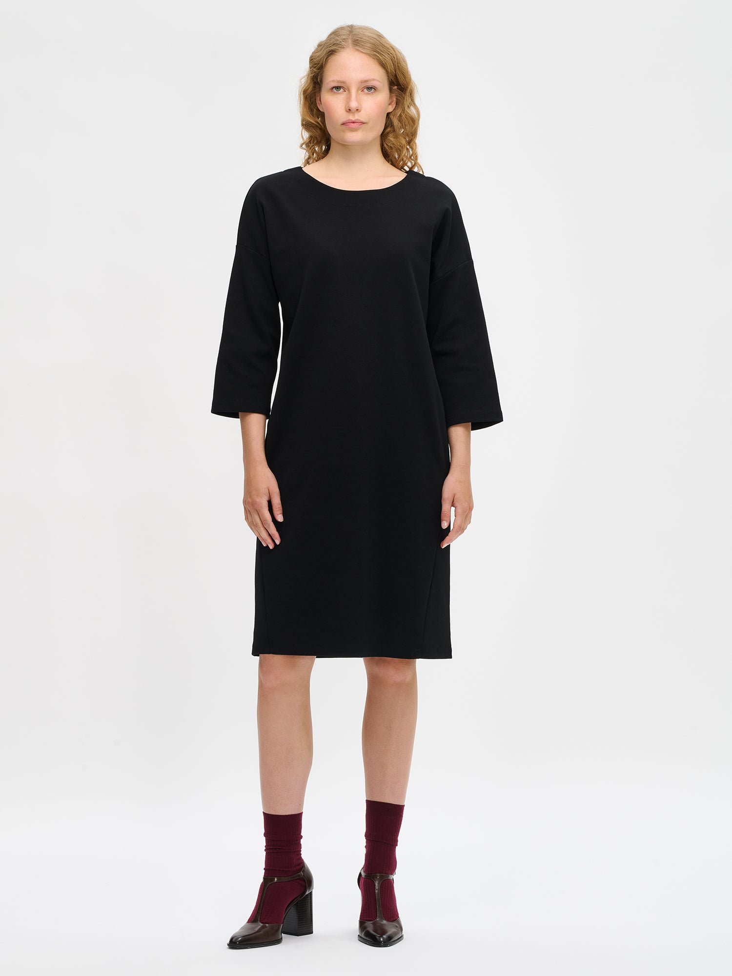 Nanso women’s black Elena knit dress in cotton–polyester–elastane, oval neckline, 3/4 sleeves and dropped shoulders, worn by model in full-body view.