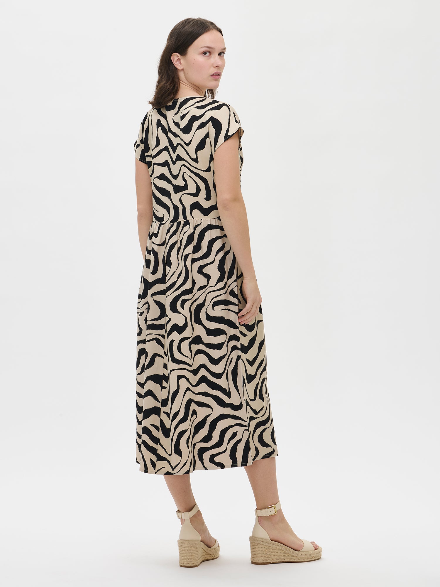 Nanso women’s patterned beige Savanna dress on the model, back view. Flowing silhouette and soft drape.