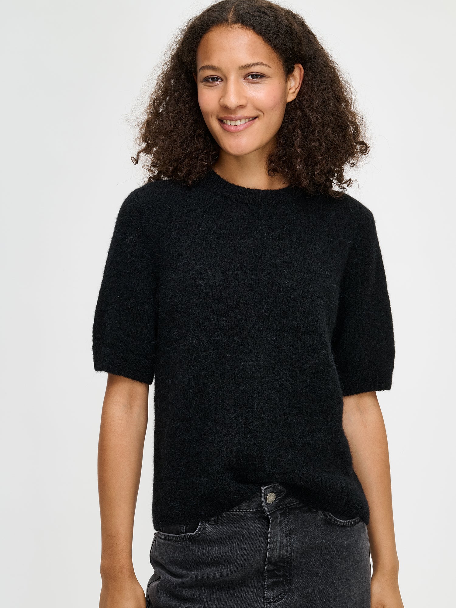 Nanso women’s Tuohi knit sweater in black, soft knit with relaxed fit, hip-length design with round neckline and short half sleeves, worn by model in close-up photo.