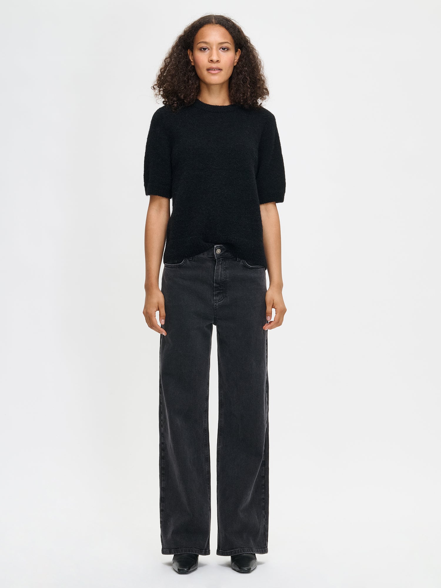Nanso women’s Tuohi knit sweater in black, hip-length style with round neckline and short half sleeves, worn by model in full-body photo.