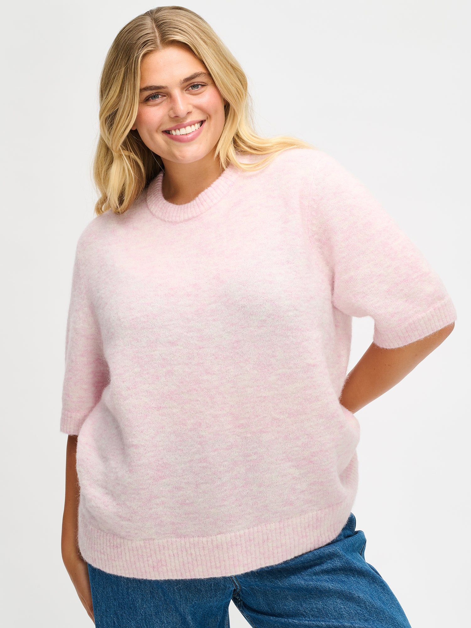 Nanso Women’s Tuohi knit sweater in pink, soft draping knit, hip-length fit with round neckline and short half sleeves, worn by plus model, size XL, in close-up photo.