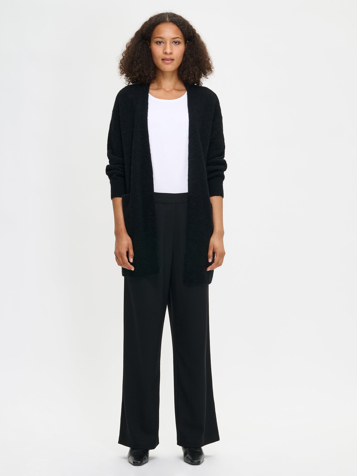 Nanso women’s black Tuohi knit cardigan, thigh-length style with long sleeves and front pockets, worn by model in full-body photo.