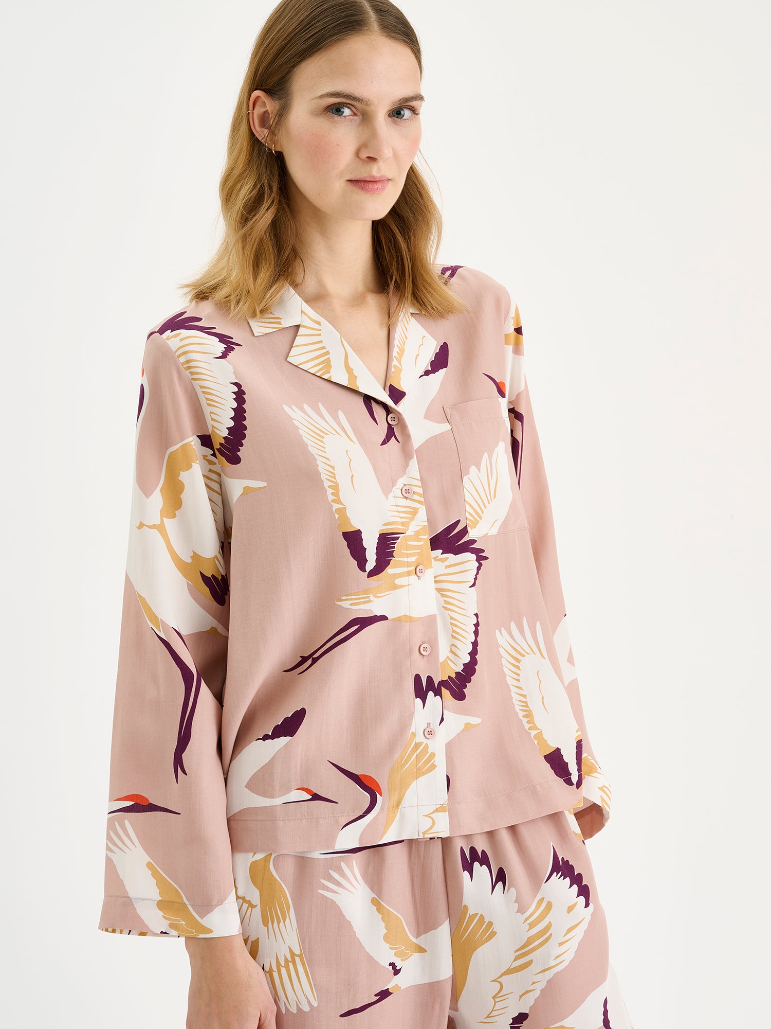 Women's elegant Kurki pajama shirt in a beautiful and striking pale pink print, on a blonde model with matching pants, close-up.