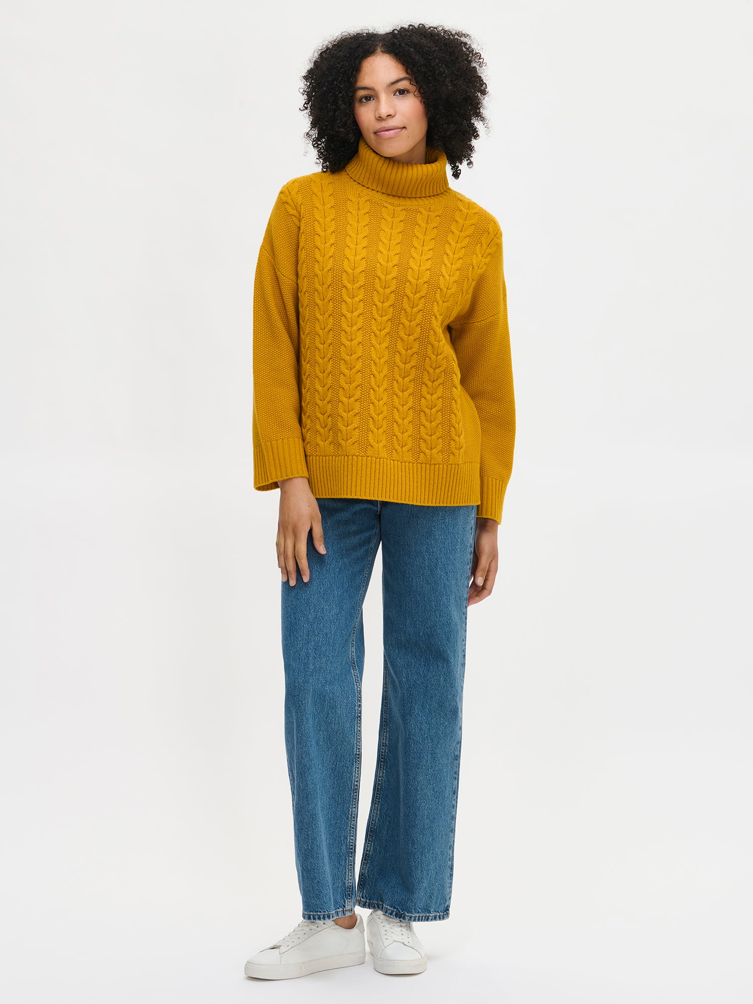 Woman wearing a yellow sweater and blue jeans on a white background