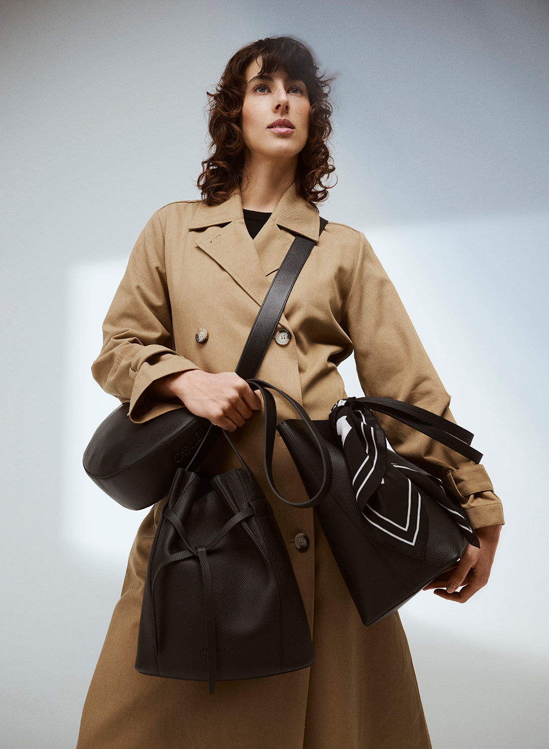 Model wearing a trench coat with black leather bags and a silk scarf