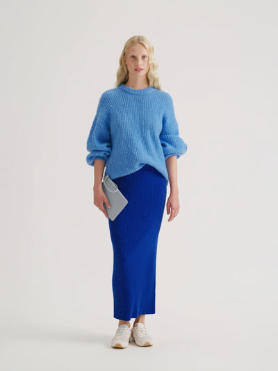 Woman wearing a light blue Karamelli knit with a blue Villis skirt