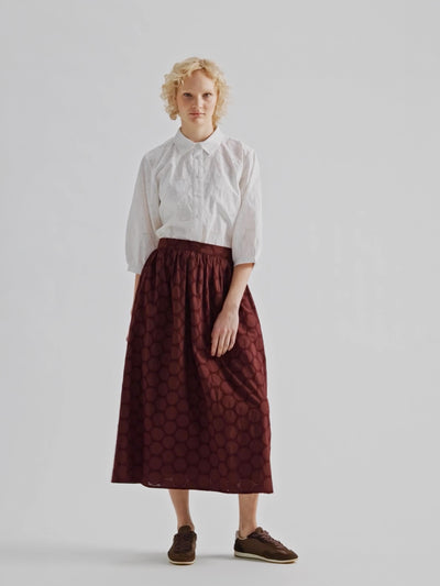 Nanso women's dark brown Siiri midi skirt, featuring a delicate lace-like woven cotton fabric with beautiful texture, pockets and a zip, on a model with a matching white Siiri blouse.